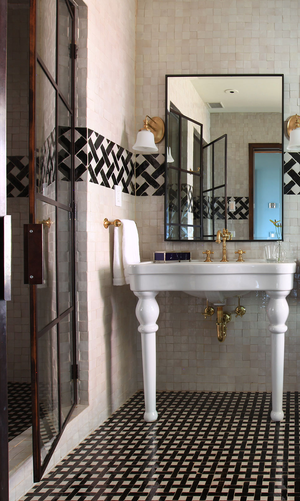 A luxurious bathroom with a white sink, gold faucet, and black and white tiles.