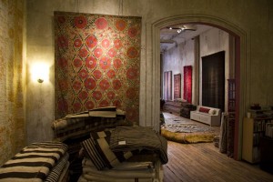 Another view of a decorative rug hanging on a wall with stacks in the foreground at Double Knot