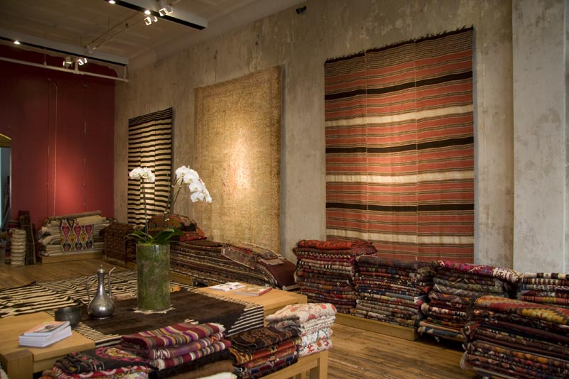 Earth toned striped and solid rugs hang behind stacks of other rugs inside Double Knot