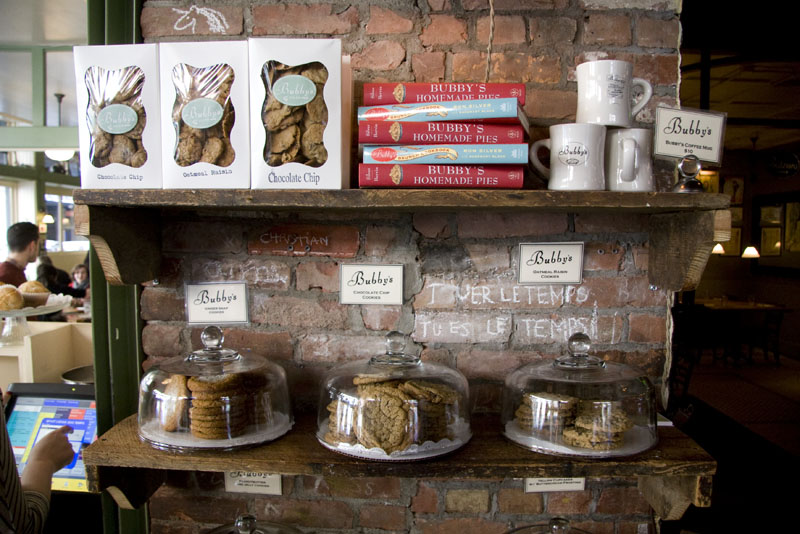 A shelf display featuring cookies, books, mugs for sale inside Bubby's Pie Company
