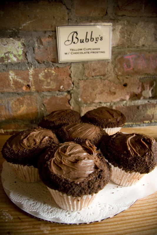 Bubby's yellow cupcakes with chocolate icing photographed against a brick wall