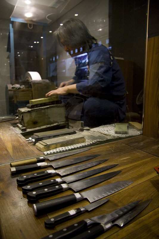 Knives laid out on a table while knife sharpening happens in the background at Korin Japanese Trading, Corp