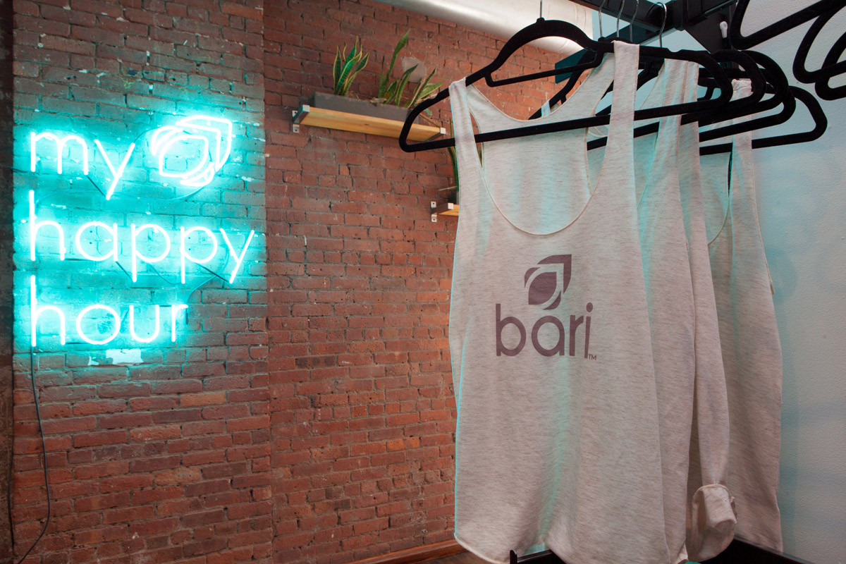 Happy hour neon sign and Bari studio tank tops handing on a retail rack