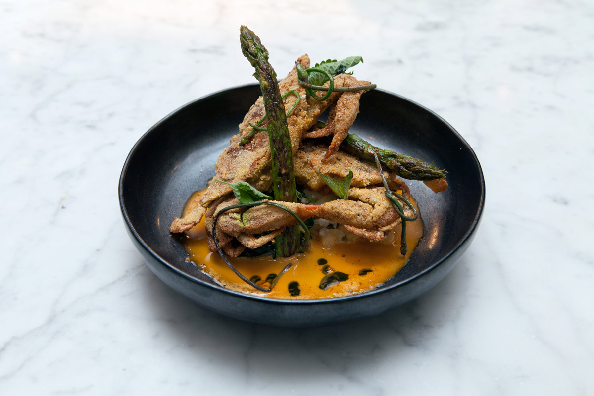 A shallow black bowl featuring a battered soft crab and asparagus at Marc Forgione