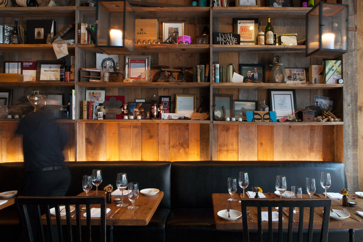 A feature wall full of shelving and decorative objects behind tables in Marc Forgione