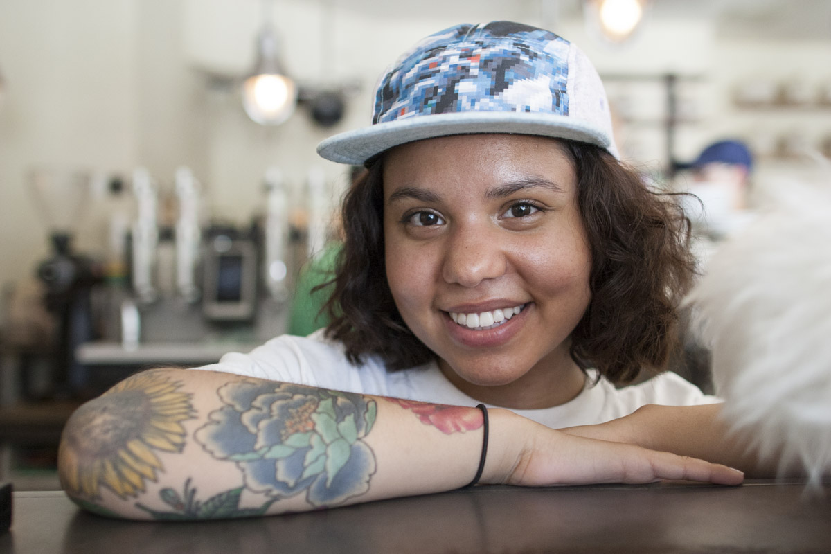 A young women with colorful tattoos on her forearm poses at the counter