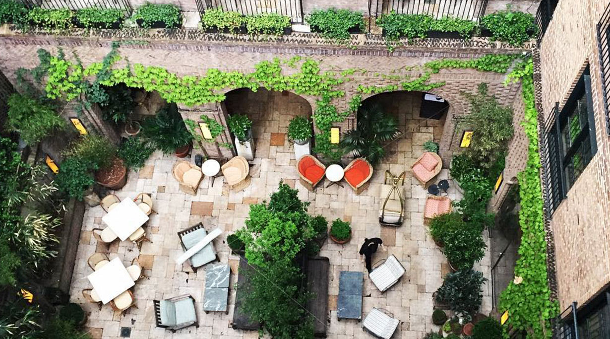 An aerial view of a courtyard with plants, seating, and brick arches.