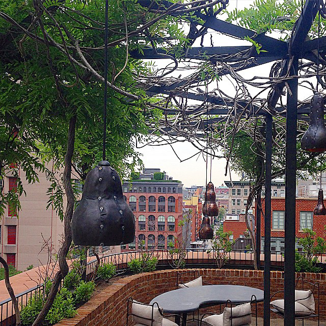A rooftop seating area with a pergola, hanging lights, and a city view.