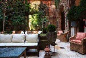 The courtyard at the Greenwich Hotel sofa and chair seating against a green and brick backdrop