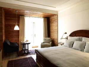 Deluxe king bed room showing part of the bed in the foreground and the wood paneling ceiling and walls in the seating area.