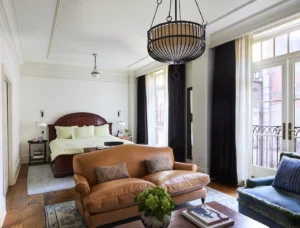 View of the Studio Suite. Looking at from the seating area, over the leather sofa and the king bed in the background. Large windows line the right wall.