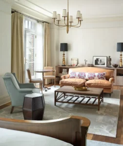 looking from the bed at the seating area. Various chairs and tables and decor create a warm atmosphere with large windows providing natural light.