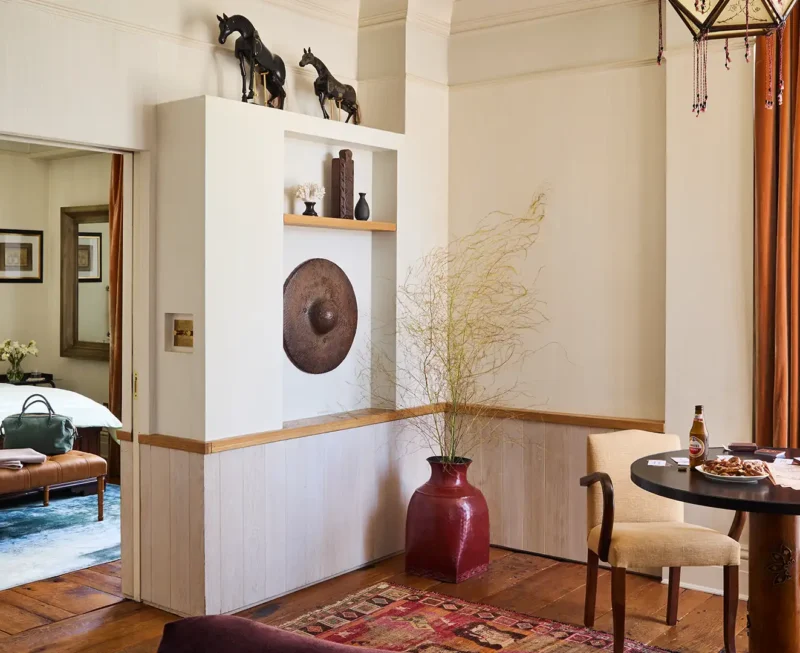 Looking from the living area into the bedroom inside the corner suite. A two seat dining table is in the lower right foreground and various decoration outline the wall separating the areas.