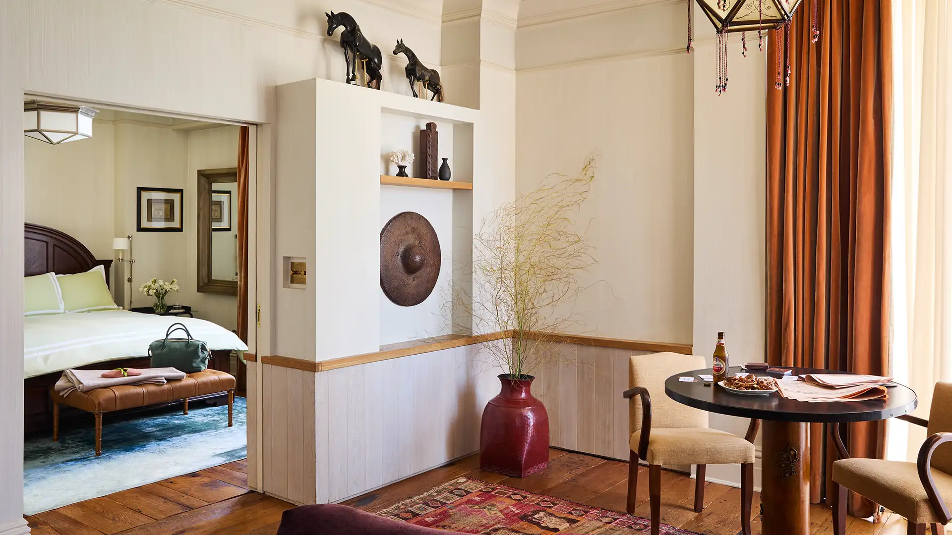 Looking from the living area into the bedroom inside the corner suite. A two seat dining table is in the lower right foreground and various decoration outline the wall separating the areas.