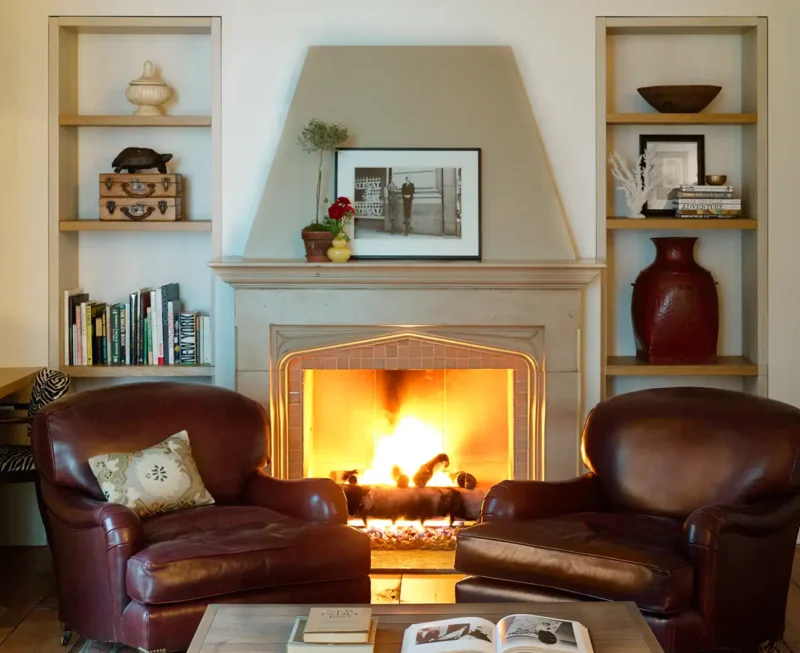 Fireplace Corner Suite looking straight on at the fireplace with active fire. Chairs and Bookshelves with decorations framing the fireplace.