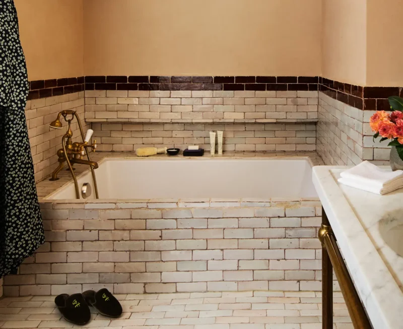 Superior King room with Soaking tub surrounding by brown and white tile. Greenwich slippers next to the tub with a robe and marble vanity.