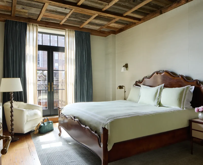 The Greenwich Duplex primary bed room featuring french doors that open to a balcony, a wood detailed ceiling, chair and king bed