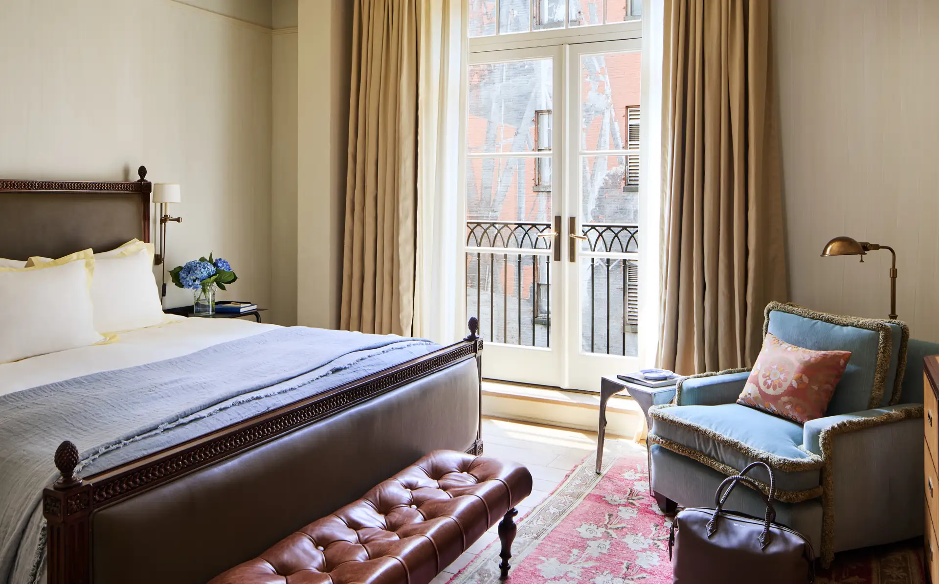 Looking at the balcony doors over the bed with an armchair in the right corner. A view of a Mural outside of the balcony doors