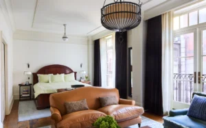View of the Studio Suite. Looking at from the seating area, over the leather sofa and the king bed in the background. Large windows line the right wall.