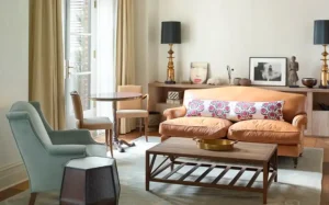 looking from the bed at the seating area. Various chairs and tables and decor create a warm atmosphere with large windows providing natural light.