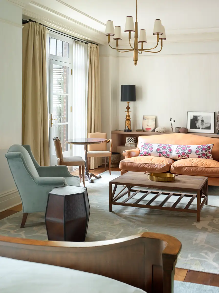 looking from the bed at the seating area. Various chairs and tables and decor create a warm atmosphere with large windows providing natural light.