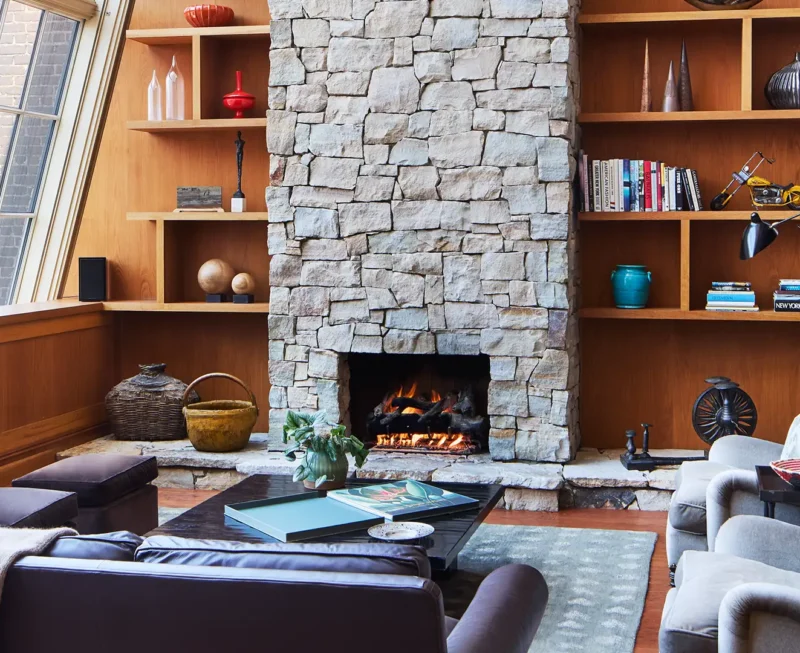 The North Moore Duplex living room area with sofas, book shelves, large windows overlooking tribeca and a stone fireplace in the middle of the photo