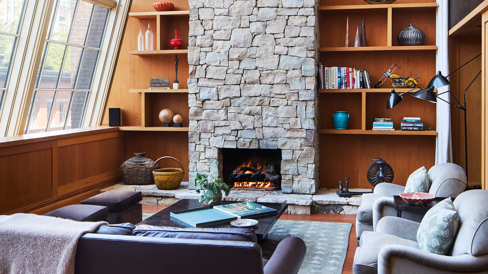 The North Moore Duplex living room area with sofas, book shelves, large windows overlooking tribeca and a stone fireplace in the middle of the photo