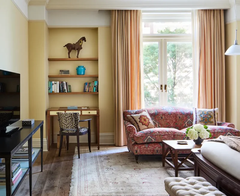 Looking at the full superior king room. A TV stand and bed appear in the foreground and sofa and desk appear against the wall with a large window.