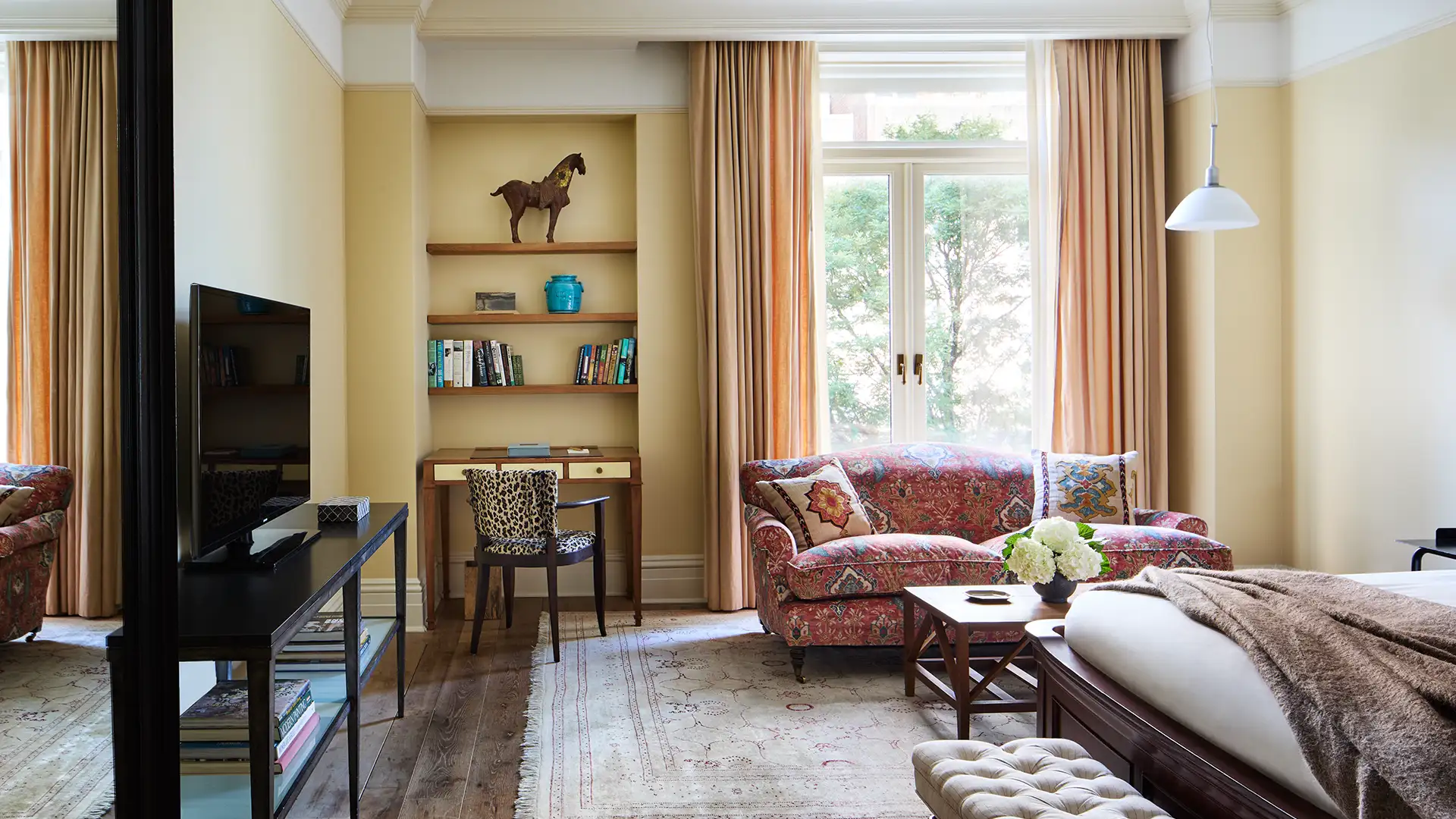 Looking at the full superior king room. A TV stand and bed appear in the foreground and sofa and desk appear against the wall with a large window.