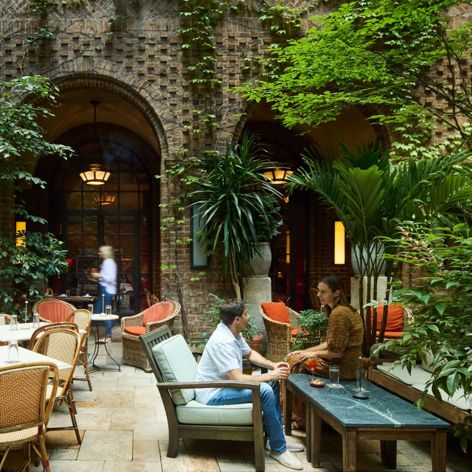 A couple casually having drinks amongst the greenery and seating inside the courtyard at the greenwich hotel