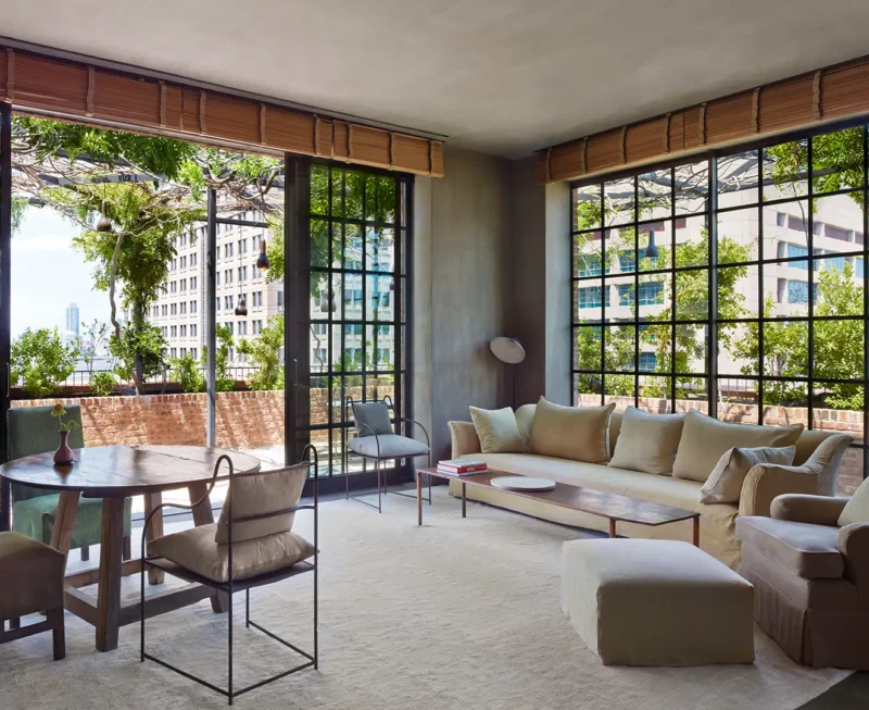 A photo of the naturally lit tribeca penthouse drawing room/seating area with table and chairs, glass doors that open to the balcony and a comfy sofa and chair